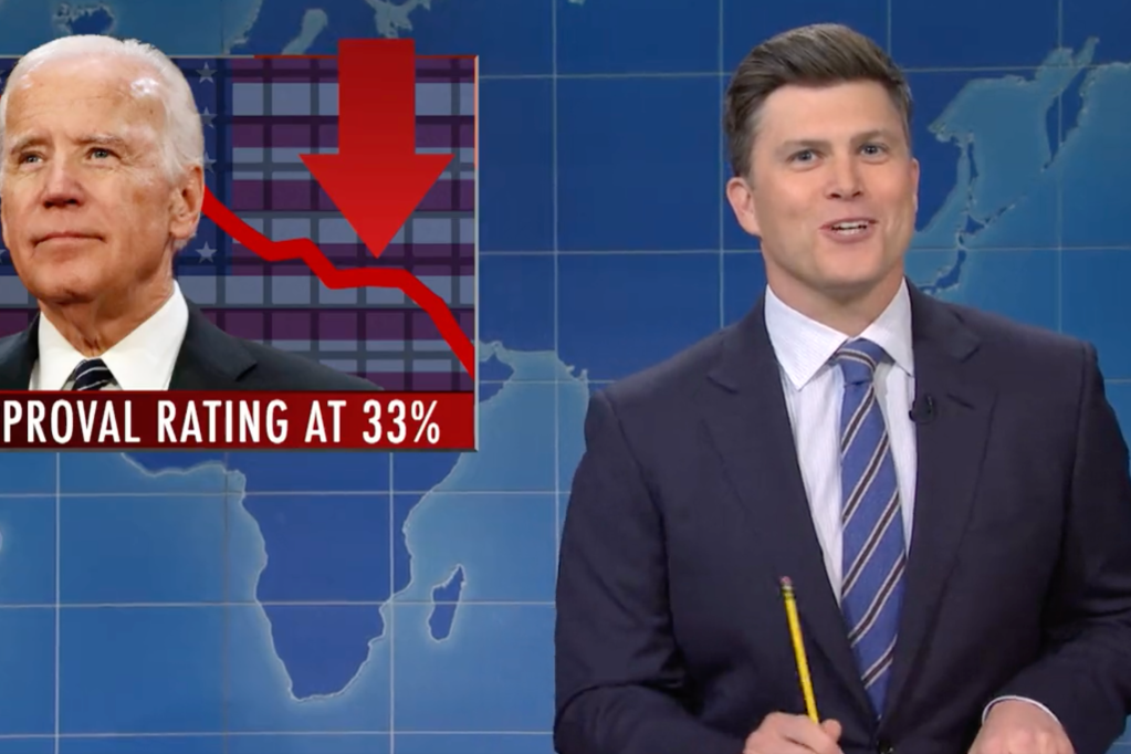 Colin Jost appears as a fake news anchor on Saturday Night Live, snapping photos of Joe Biden and referring to Kamala Harris.