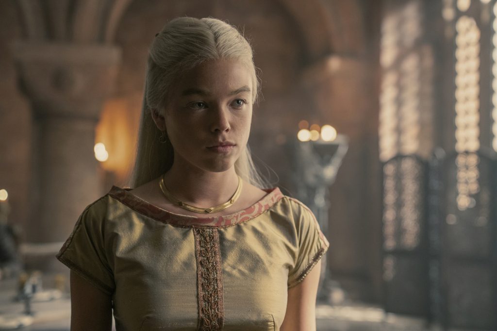 Millie Alcock as Princess Rhaenyra Targaryen in "Dragon House" Standing in a room, wearing a dress. 