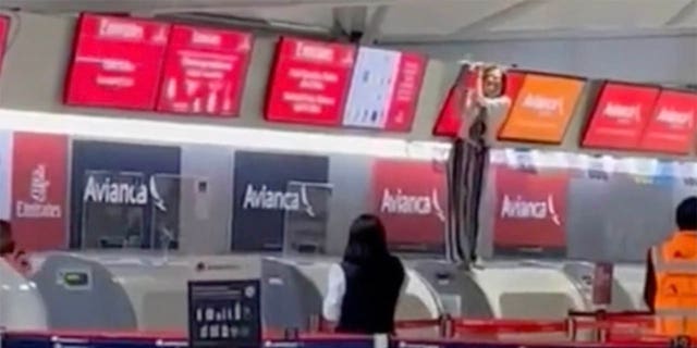Other passengers at the airport can see the out-of-control person - standing at the check-in counter and holding a screen over it - from afar.