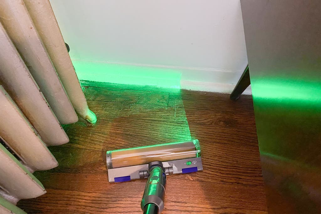 A Dyson V12 shines a green light on a dusty corner of the floor.